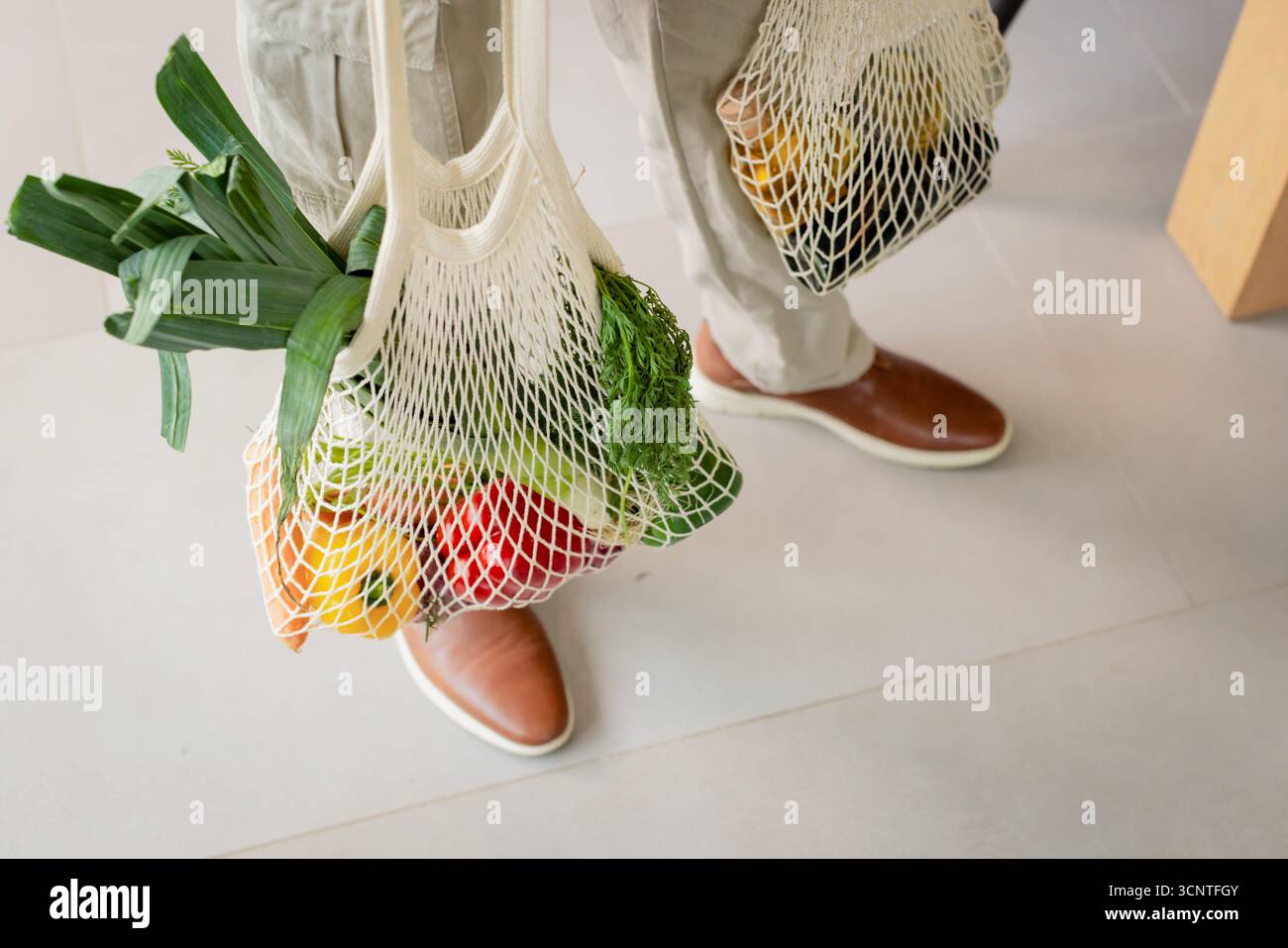 Afroamerikaner, der auf grauem Fliesenboden steht und weißes Netztuch mit Produkten hält Stockfoto