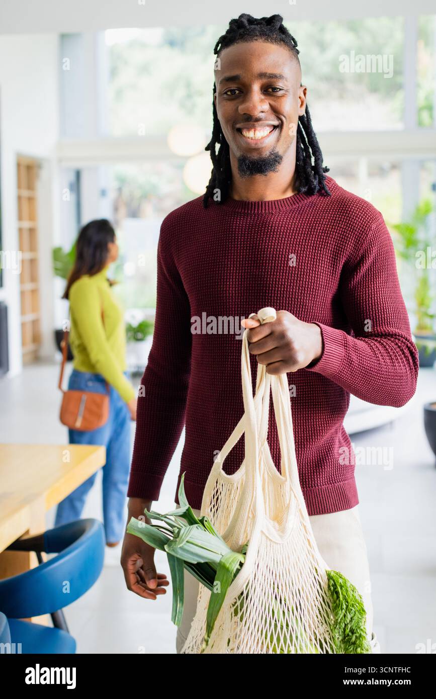 Diverse Paare, die in der modernen Küche wiederverwendbare Lebensmittelbeutel aus Mesh mit Blattgemüse tragen Stockfoto