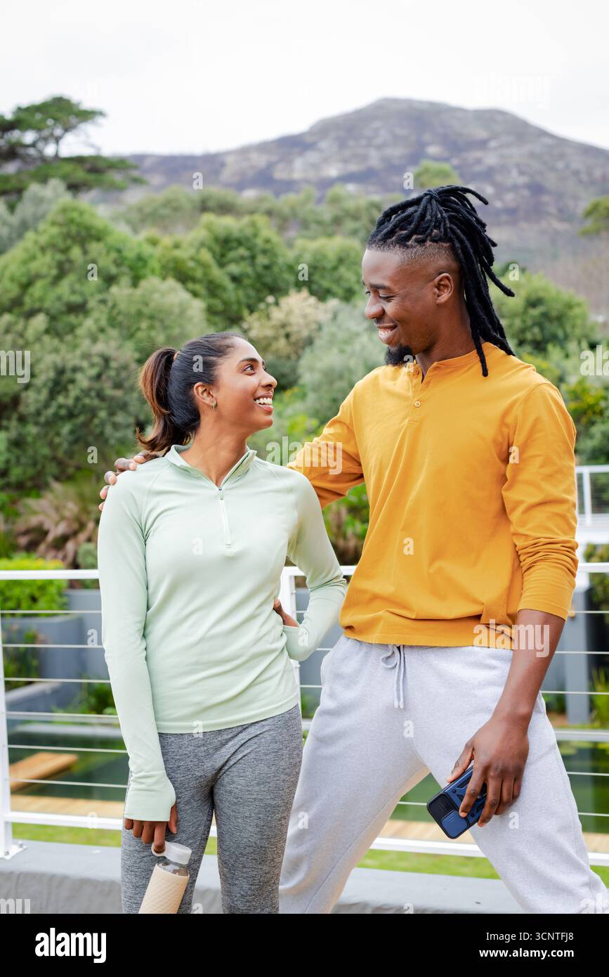 Verschiedene Paare stehen auf dem Balkon mit Blick auf den Hügel, während sie eine Wasserflasche und ein Smartphone in der Hand halten Stockfoto