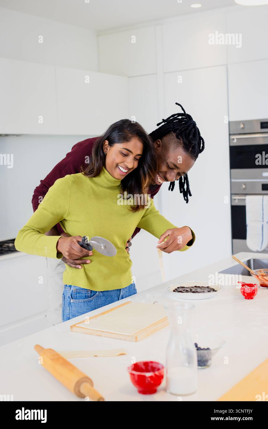 Diverse Paare schneiden Pizzateig mit Pizzaschneider auf der Arbeitsplatte Insel in moderner Küche Stockfoto