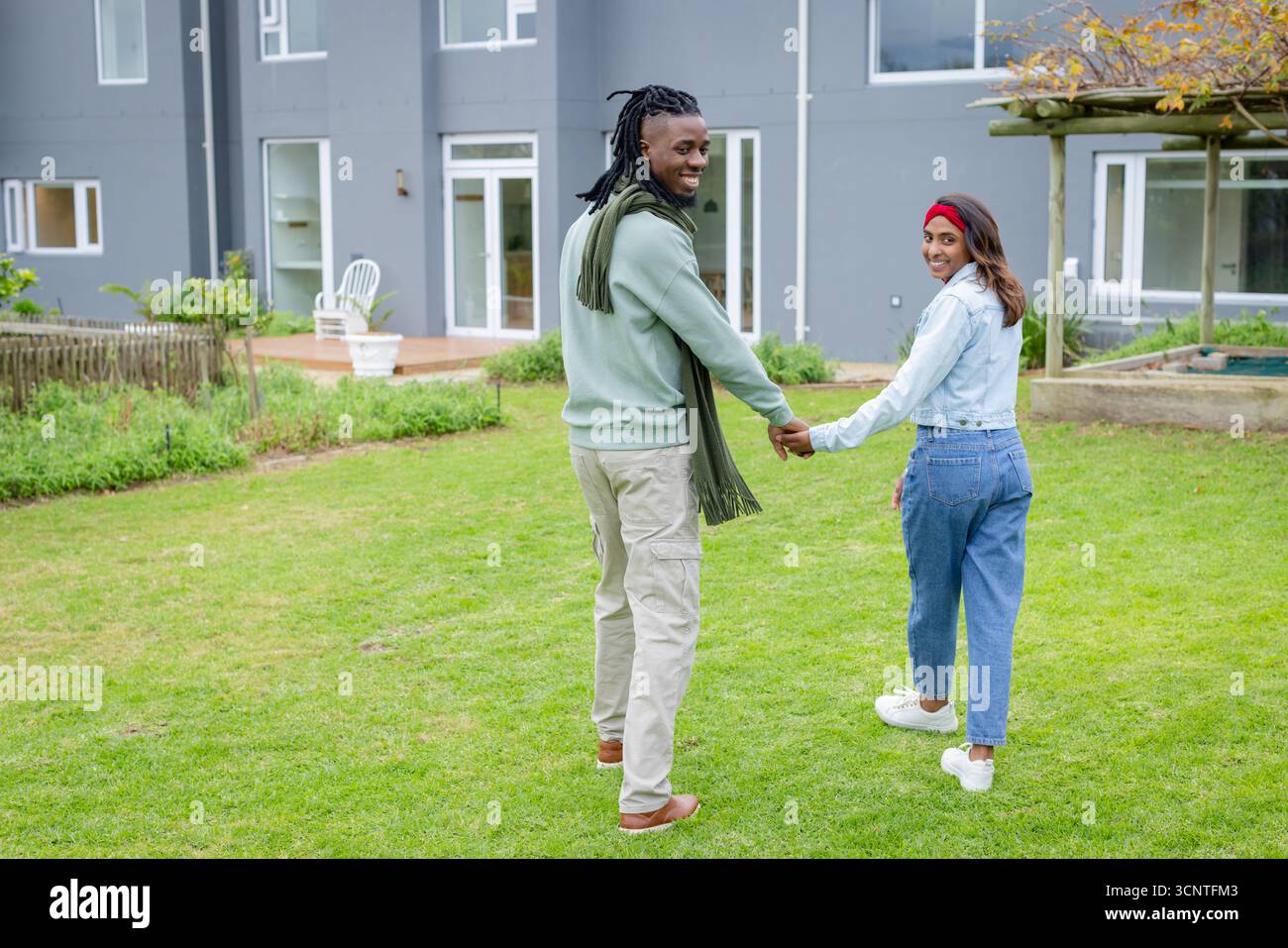 Verschiedene Paare gehen Hand in Hand über grünen Rasen in Richtung eines modernen grauen Gebäudes mit weißem Stuhl Stockfoto