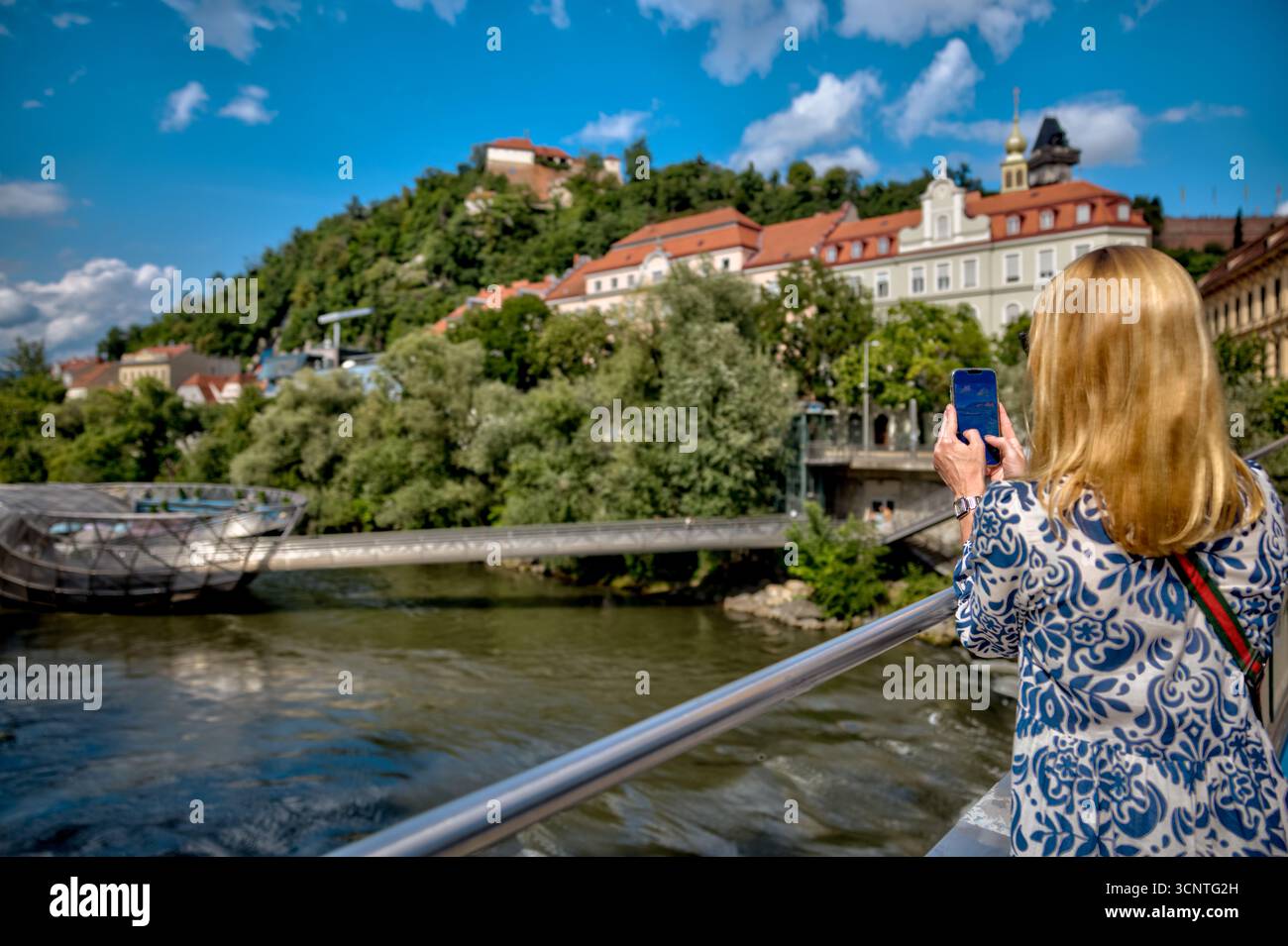 Ein Tourist fotografiert die berühmte Murinsel und den Schlossberg in Graz Stockfoto