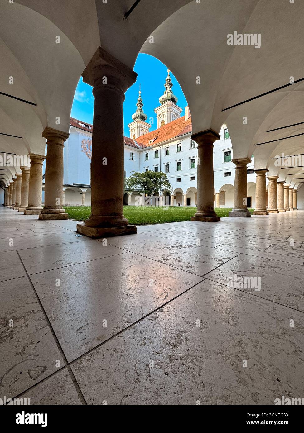 Steinsäulen und Gewölbebögen säumen den Innenhof des historischen Franziskanerklosters bei der Mariahilferkirche, Teil eines Jahrhunderte alten Komplexes in Gr Stockfoto
