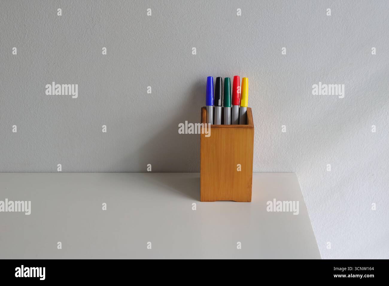 Stifthalter aus Holz mit verschiedenen Farbstiften, die auf einer Seite des weißen Holztischs platziert werden Stockfoto