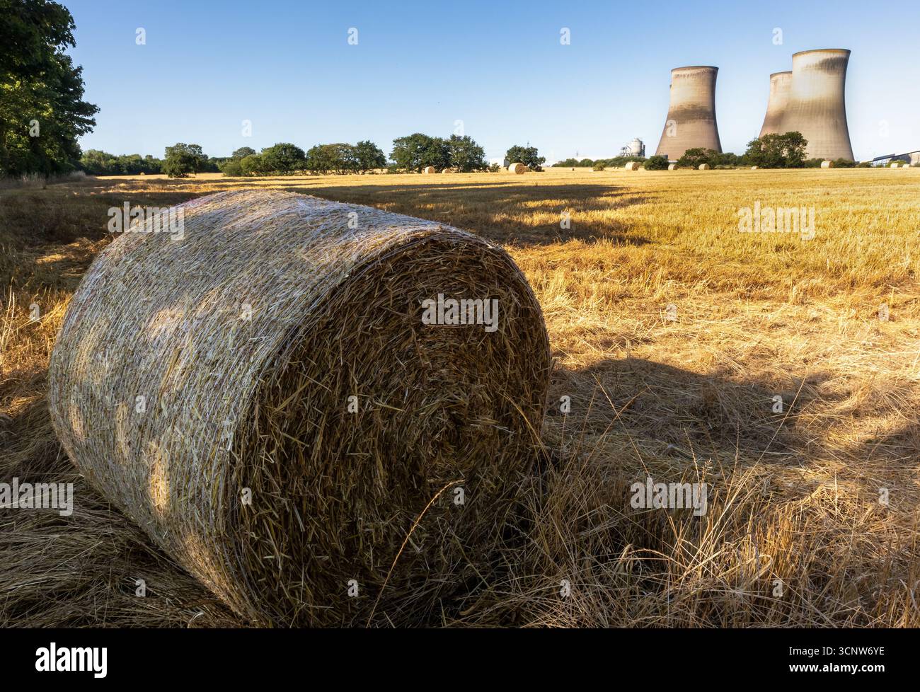 Heuballen auf dem geernteten Feld mit den Kühltürmen der Fiddler’s Ferry Power Station im Hintergrund Stockfoto
