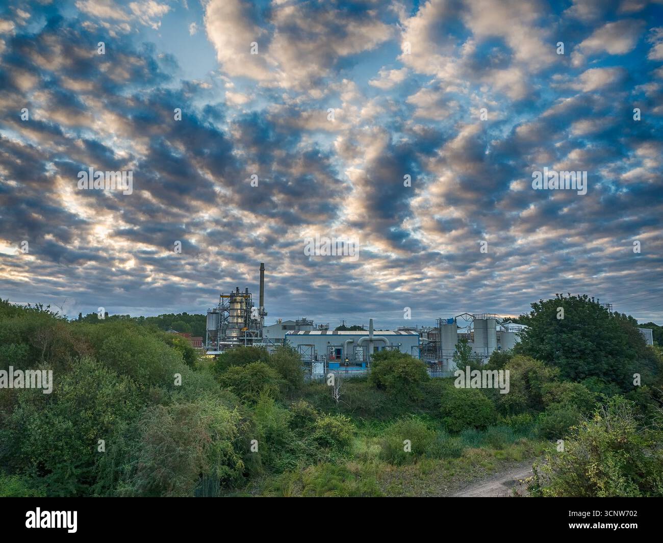 Industrieanlagen und Fabrikgebäude mit dramatischer Wolkenlandschaft darüber Stockfoto