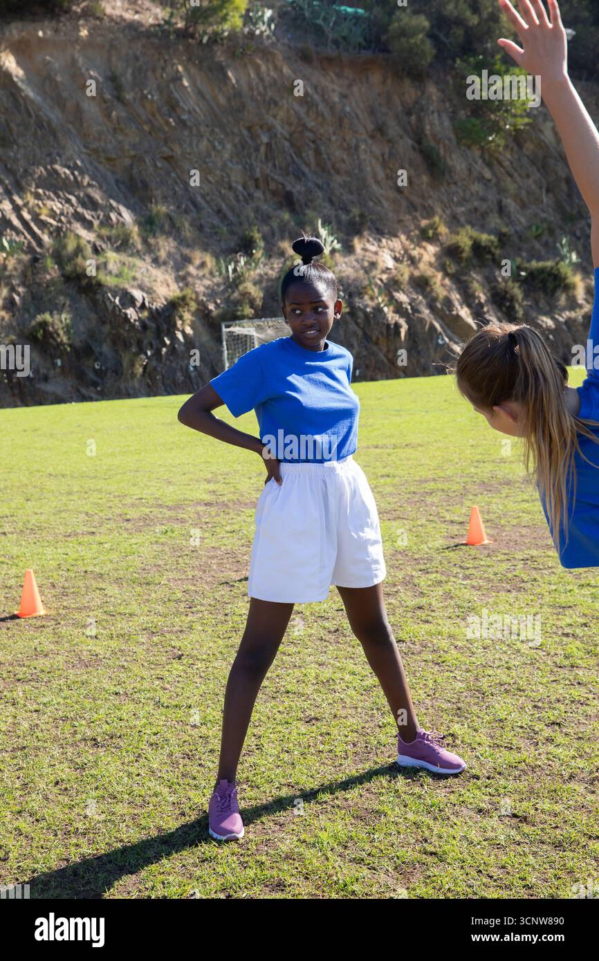 Verschiedene weibliche Teenager-Athleten üben Übungen auf dem Feld mit Kegeln und Fußballtor Stockfoto