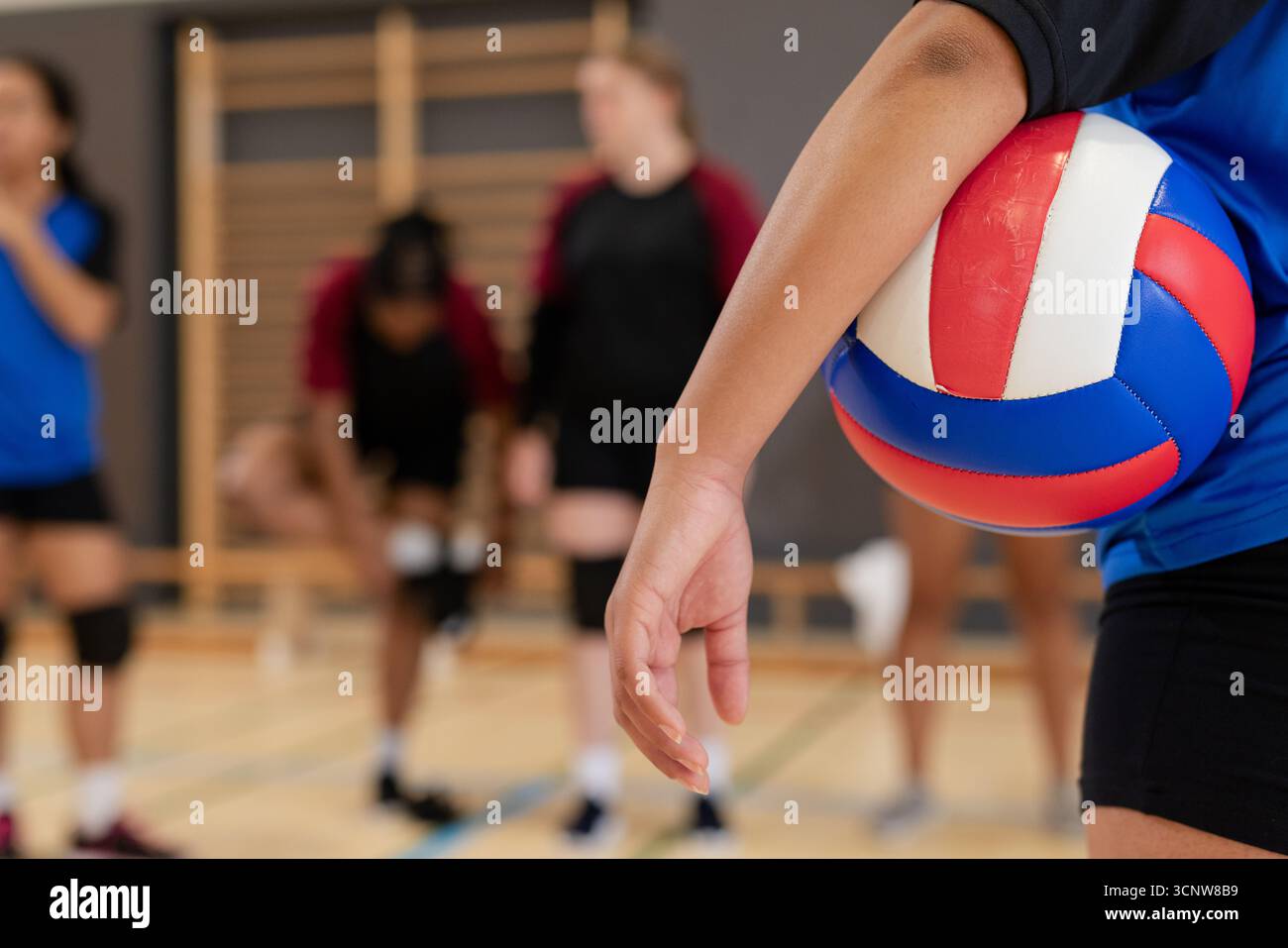 Asiatisch-indische Volleyballspielerin, die im Fitnessstudio rot-blauen Ball in Trikot serviert, Kopierraum Stockfoto