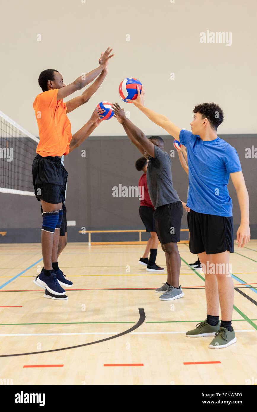 Verschiedene männliche Athleten in Sportbekleidung üben Blocktraining im Fitnessstudio mit Volleyballnetz, Bälle Stockfoto