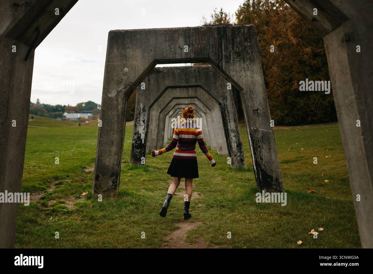 Eine junge Frau in einem farbenfrohen Pullover spaziert durch eine geometrische Architektur in einem Seattle Park. Umgeben von Herbstlaub, die Szene Captu Stockfoto