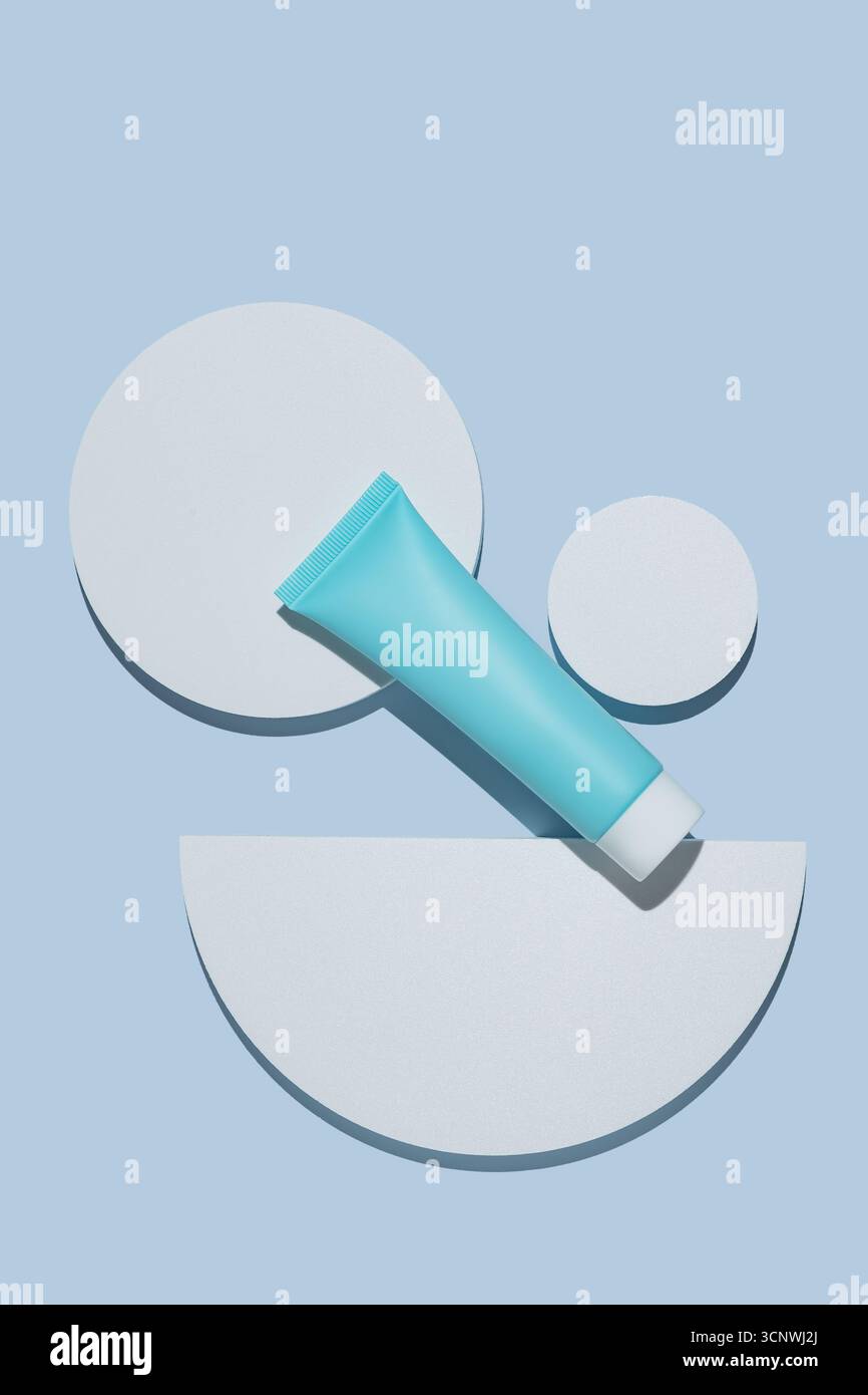 Ein schickes Kosmetikpaket mit blauer Röhre auf minimalistischem blauem Hintergrund mit geometrischen weißen Formen. Ideal für moderne Hautpflege- oder Schönheitsprodukte Stockfoto