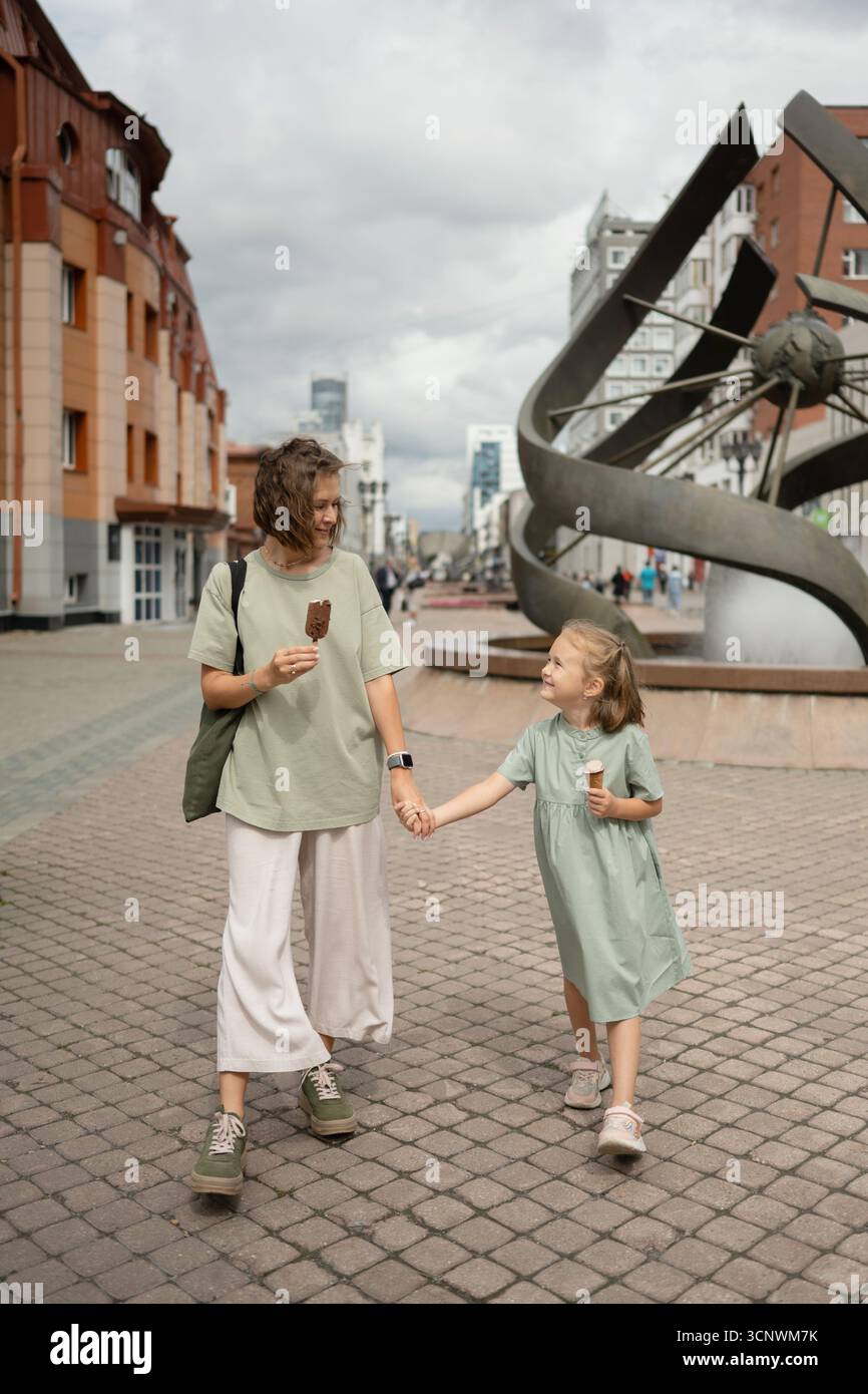 Eine Mutter und Tochter genießen einen Sommertag in der Stadt mit Eis und Lachen. Sie halten die Hände und fangen das Wesen von Familienbindung und Chi ein Stockfoto