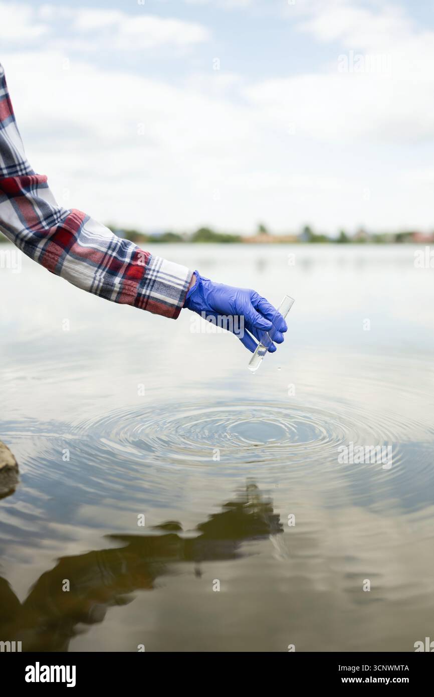 Eine junge Biologin, die Handschuhe trägt, sammelt Wasserproben aus einem ruhigen See. Sie führt Analysen zur ökologischen Forschung an Naturwasser qu durch Stockfoto
