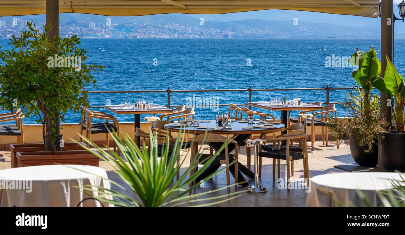 Terrasse des Restaurants am Meer mit Meerblick, Esstisch im Freien und Skyline der Stadt in Opatija Kroatien. Stockfoto