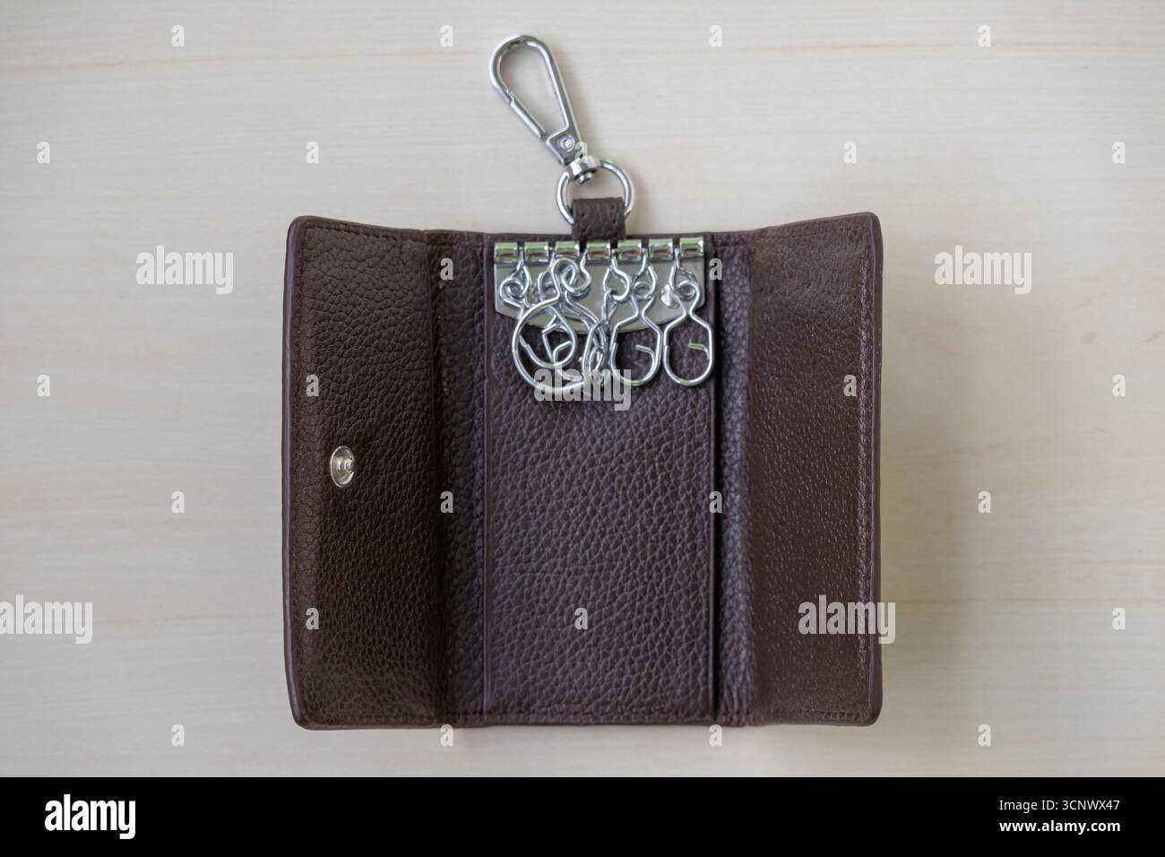 Geöffneter Schlüsselhalter aus Leder auf hellbraunem, strukturiertem Hintergrund. Ledertasche zur Aufbewahrung von Schlüsseln, Innenansicht. Stockfoto