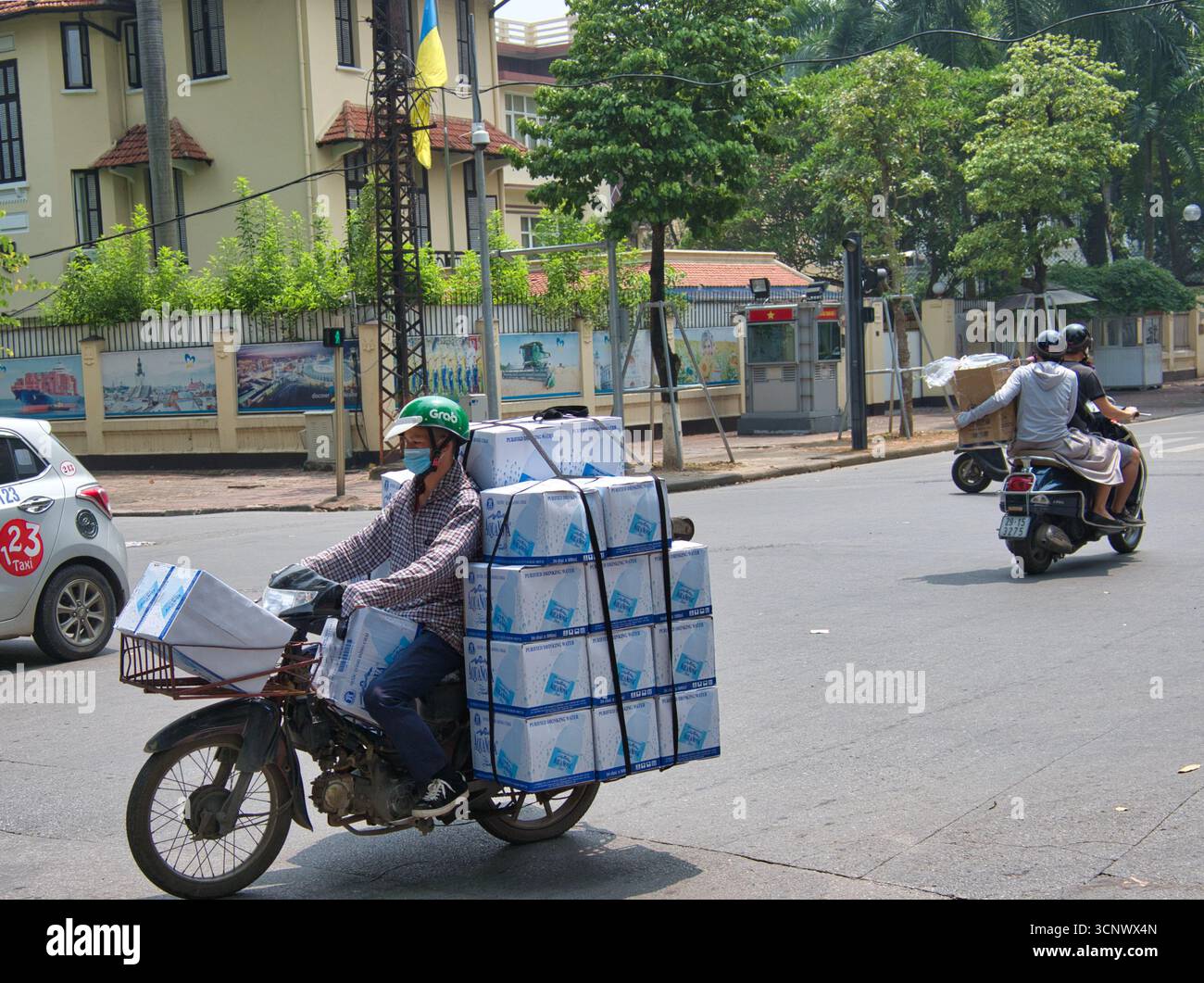 Zustellfahrer mit Kisten auf einem Moped - Ein Zustellfahrer auf einem Moped, beladen mit vielen großen Kisten, ein typischer Anblick von Transport und Handel auf einem Stockfoto