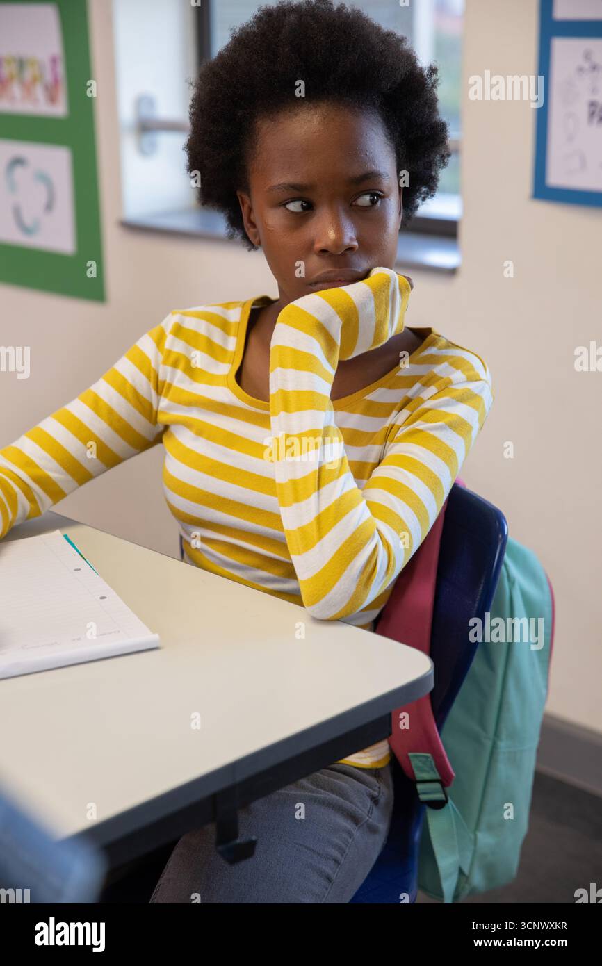 afroamerikanischer Teenager-Student sitzt und blickt direkt auf den Schreibtisch mit Notizbuch und Rucksack Stockfoto