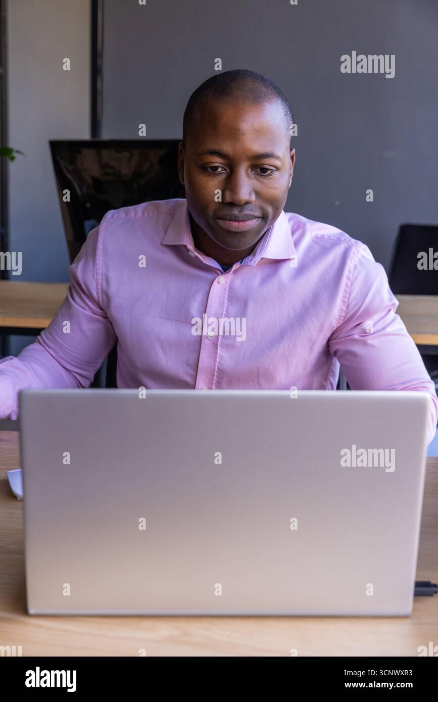 Ein afroamerikanischer Mann, der am Schreibtisch arbeitet und ein rosafarbenes Hemd in der Nähe des Stromkabels trägt Stockfoto