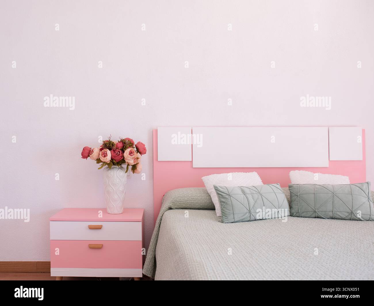 Das moderne Schlafzimmer verfügt über ein pinkfarbenes Kopfteil und einen passenden Nachttisch, ergänzt durch eine Vase aus Rosen, die den ruhigen und stilvollen Ambi unterstreicht Stockfoto