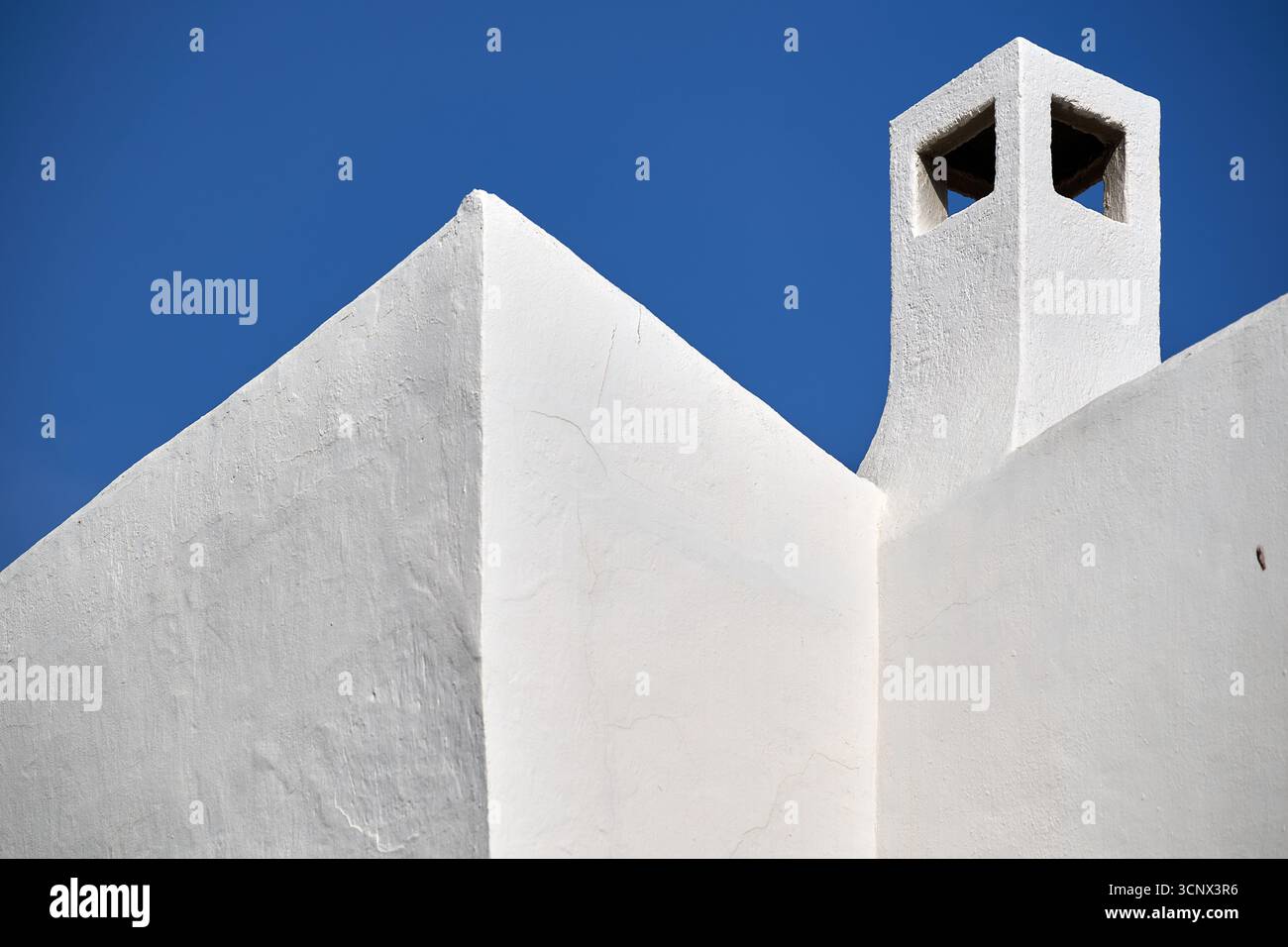 Weißer moderner Kamin auf geometrischem Gebäude vor blauem Himmel, Altea Spain, minimalistische horizontale Komposition, sauberes Design, architektonische Ästhetik, c Stockfoto