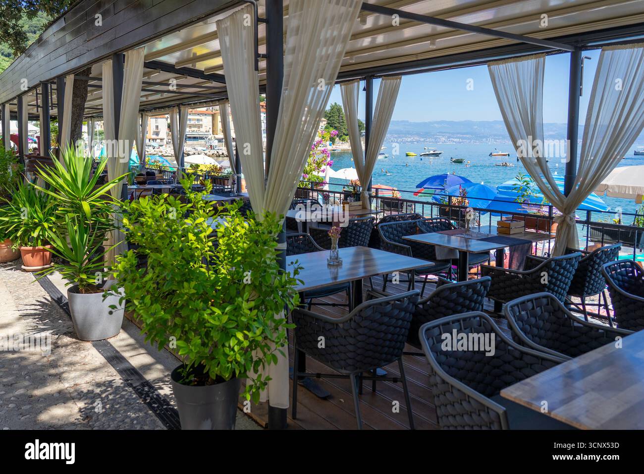 Cafe-Terrasse am Meer mit Tischen und Meerblick, Sonnenschirme und Boote in der Nähe. Stockfoto