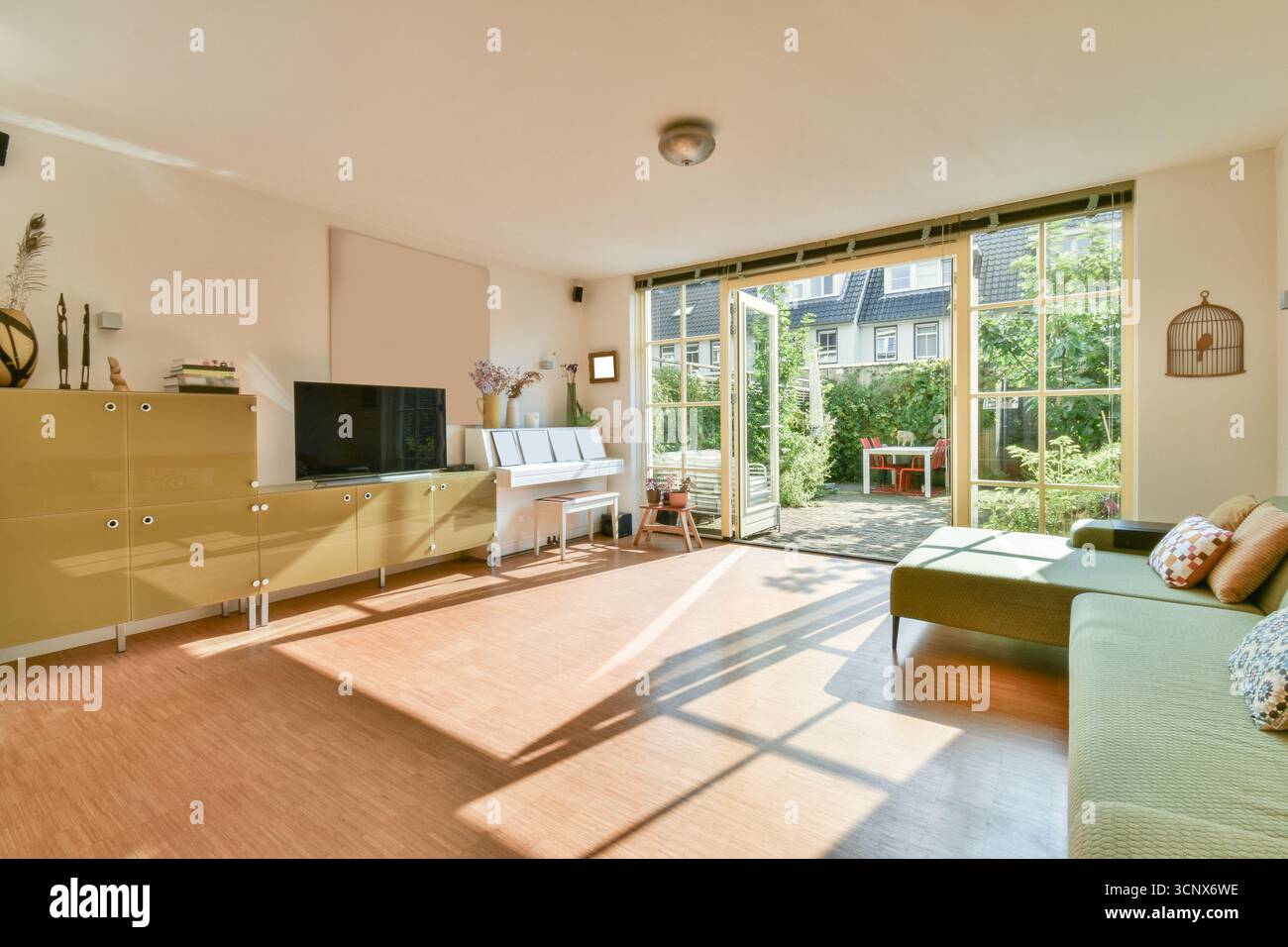 Ein geräumiges, modernes Wohnzimmer mit Sonnenlicht, das durch große Fenster strömt, üppigem Grün, das draußen sichtbar ist, und gemütlichen Möbeln, die eine warme Atmosphäre schaffen Stockfoto