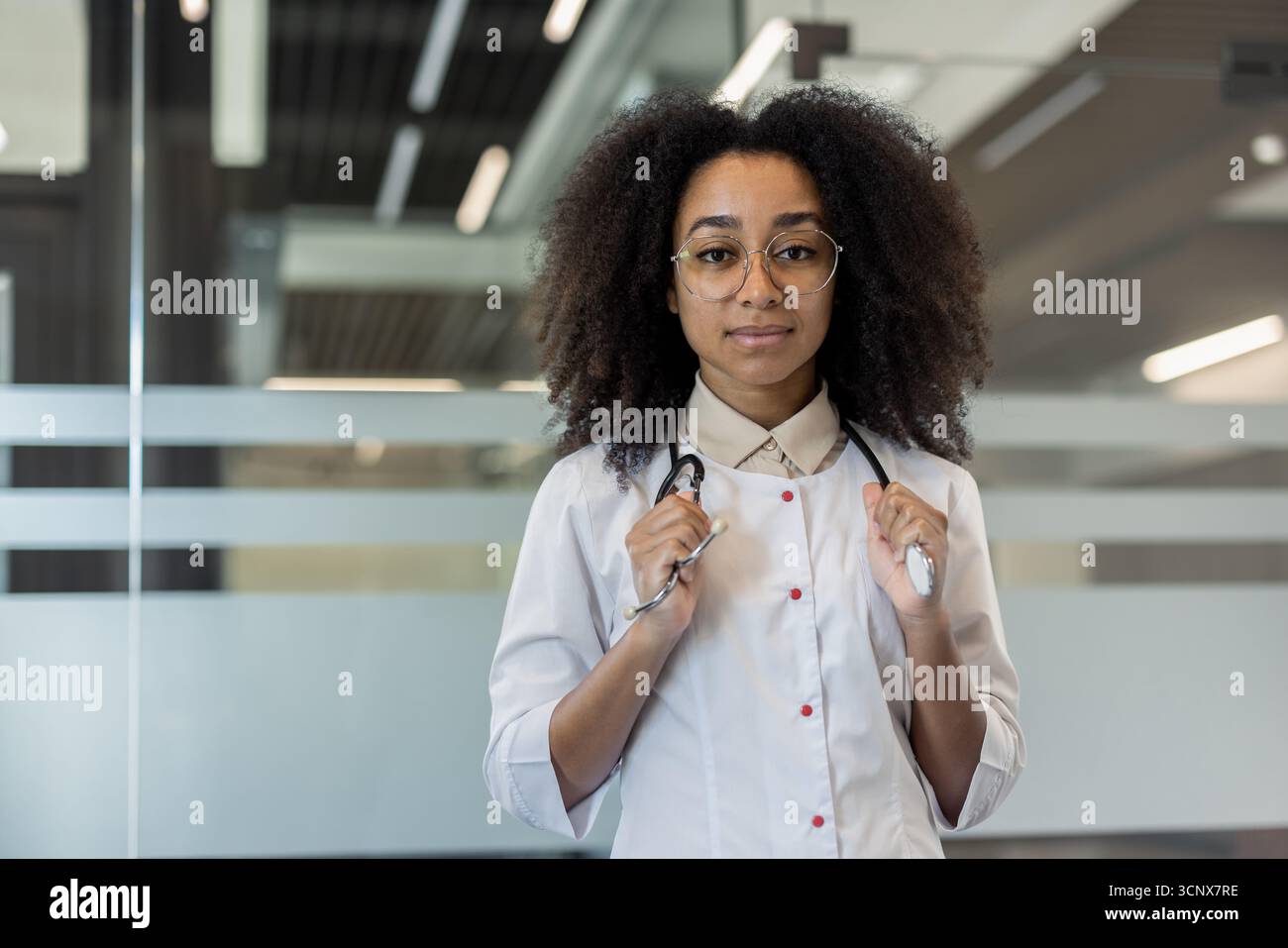 Porträt einer ernsthaften jungen afroamerikanischen Ärztin, Wissenschaftlerin, Apotheker, die in Uniform in der Klinik steht, das Stethoskop in den Händen hält und selbstbewusst in die Kamera blickt. Stockfoto