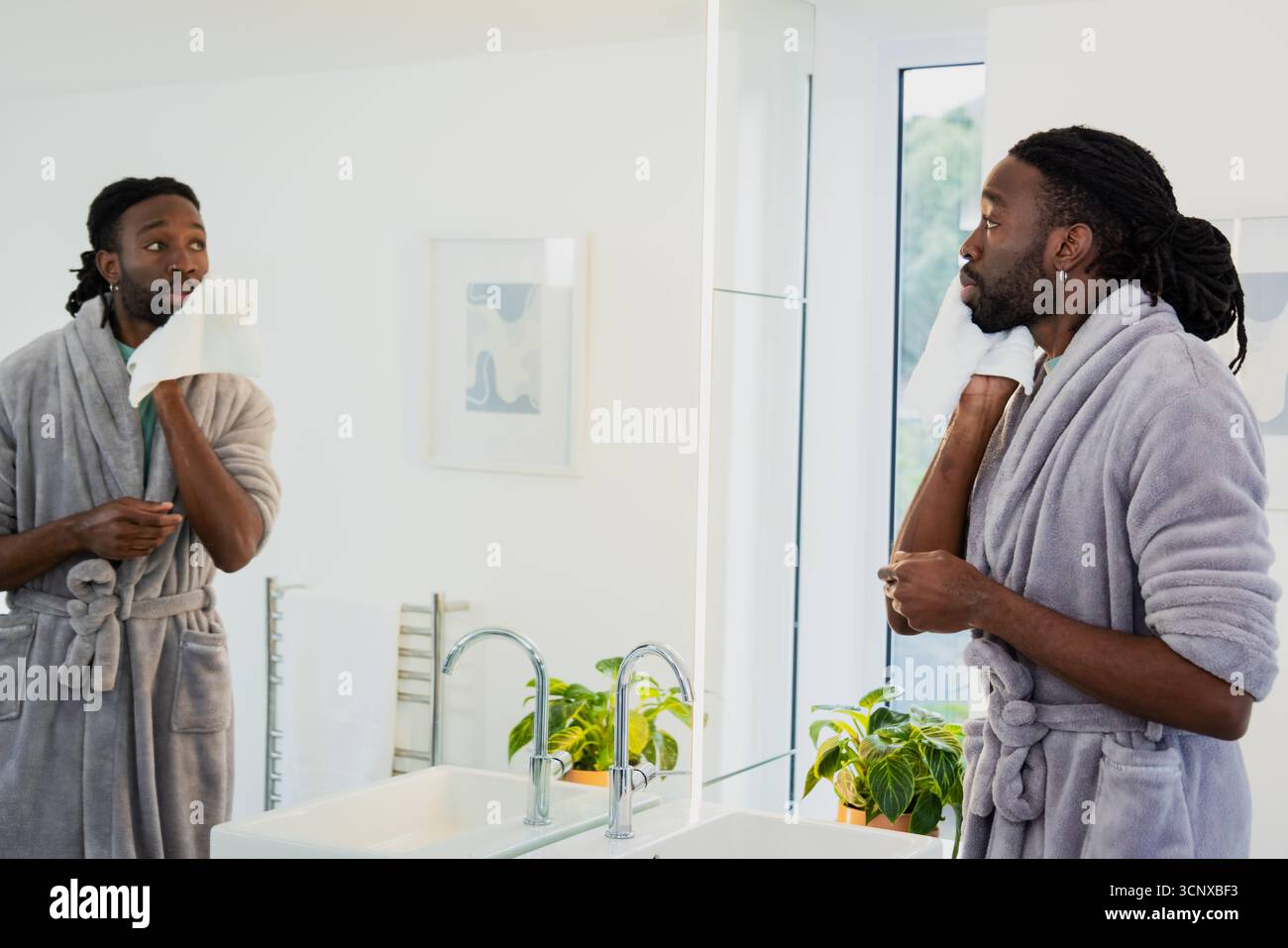 Afroamerikanischer Mann mit Bademantel, trocknendem Gesicht und weißem Handtuch am Badezimmerspiegel, Kopierraum Stockfoto