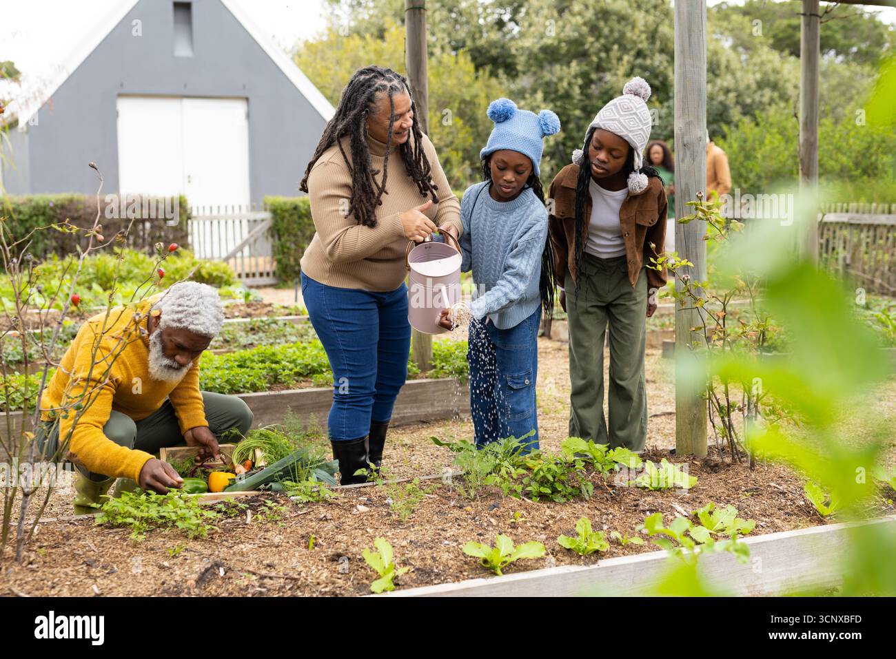 Vielfältige, generationenübergreifende Familie, die auf Hochbeeten im Hinterhof mit rosafarbener Gießkanne arbeitet Stockfoto