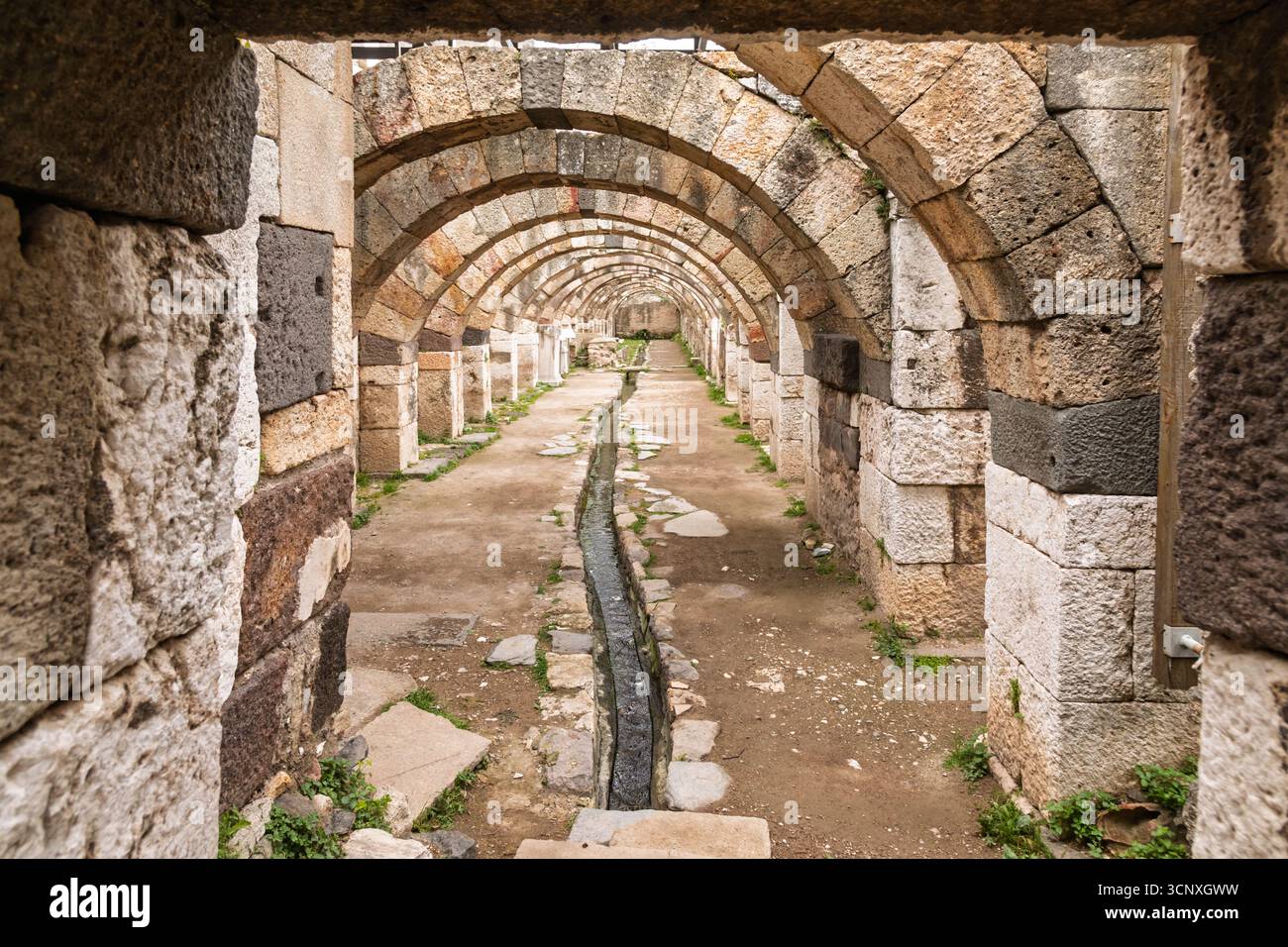 Eine gut erhaltene Reihe römischer Steinbögen und ein zentraler Entwässerungskanal säumen den inneren Gang der Agora von Smyrna in Izmir, Türkei, showca Stockfoto