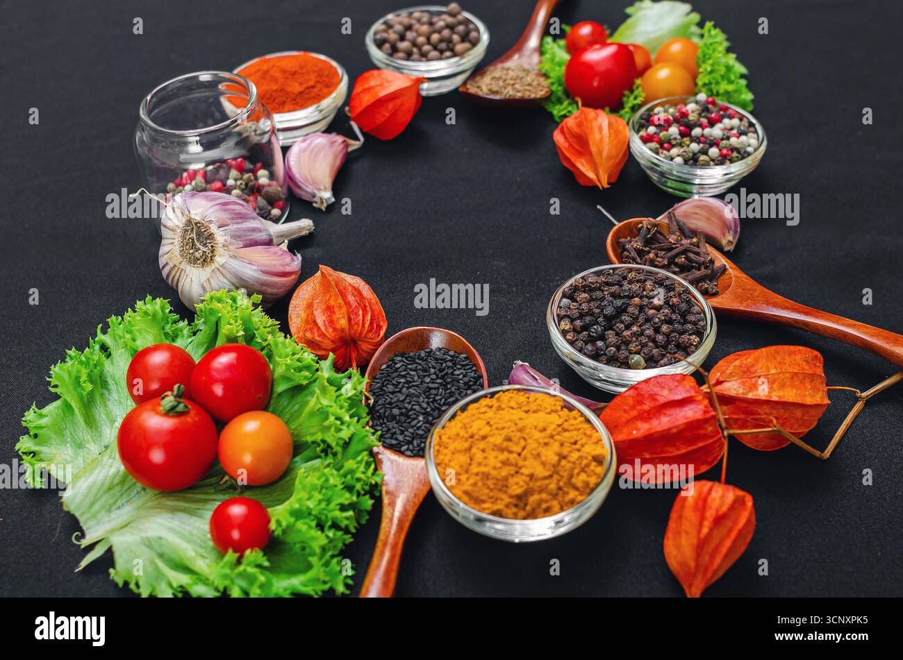 Helle aromatische trockene Gewürze und Gewürze, frisches Gemüse, Holzlöffel zum Kochen auf schwarzem Hintergrund in Form von Rahmen. Bio-Inhaltsstoffe für die Heilung Stockfoto