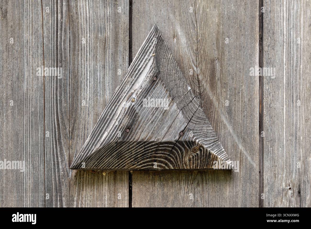 Ein verwittertes Holzdreieck sitzt auf grauen Dielen und zeigt natürliche Körnung und robuste Textur. Ideal für rustikale Einrichtung, Kunsthandwerk, Hintergründe und se Stockfoto Ein verwittertes Holzdreieck sitzt auf grauen Dielen und zeigt natürliche Körnung und robuste Textur. Ideal für rustikale Einrichtung, Kunsthandwerk, Hintergründe und se Stockfoto
