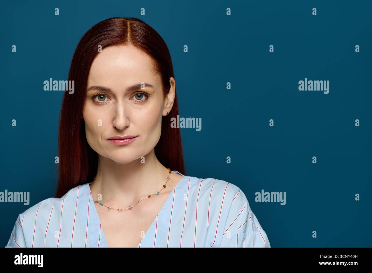Eine selbstbewusste Frau mit rotem Haar posiert anmutig vor einem beruhigenden blauen Hintergrund. Stockfoto
