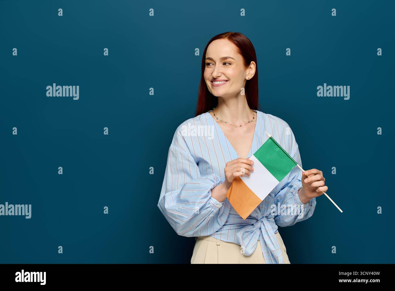 Ein fröhlicher Sprachlehrer mit roten Haaren hält eine Flagge, während er in einem blauen Studio steht. Stockfoto