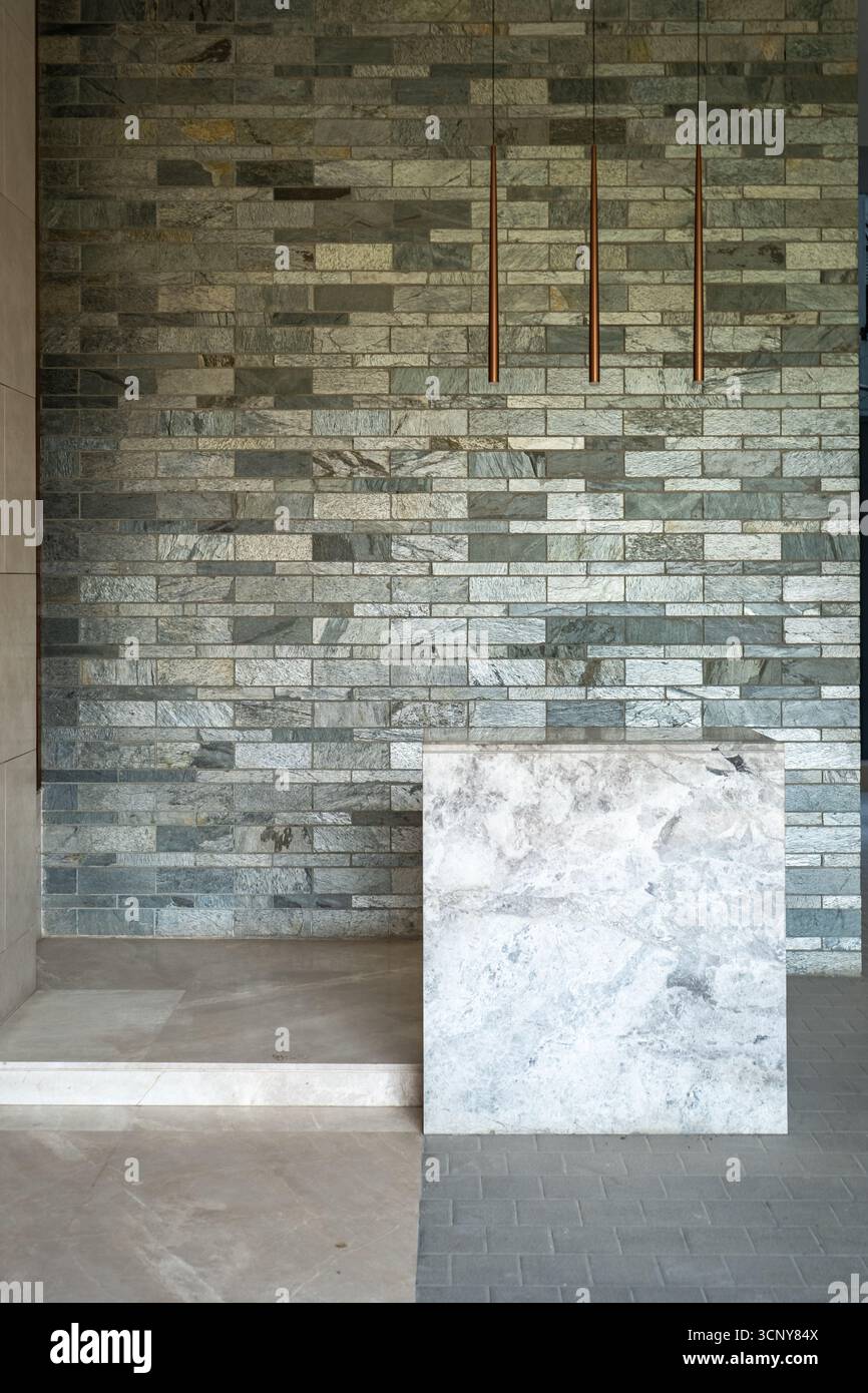 Ein eleganter, minimalistischer Rezeptionstresen aus Marmor und Stein mit drei hängenden Hängelampen aus Kupfer. Stockfoto