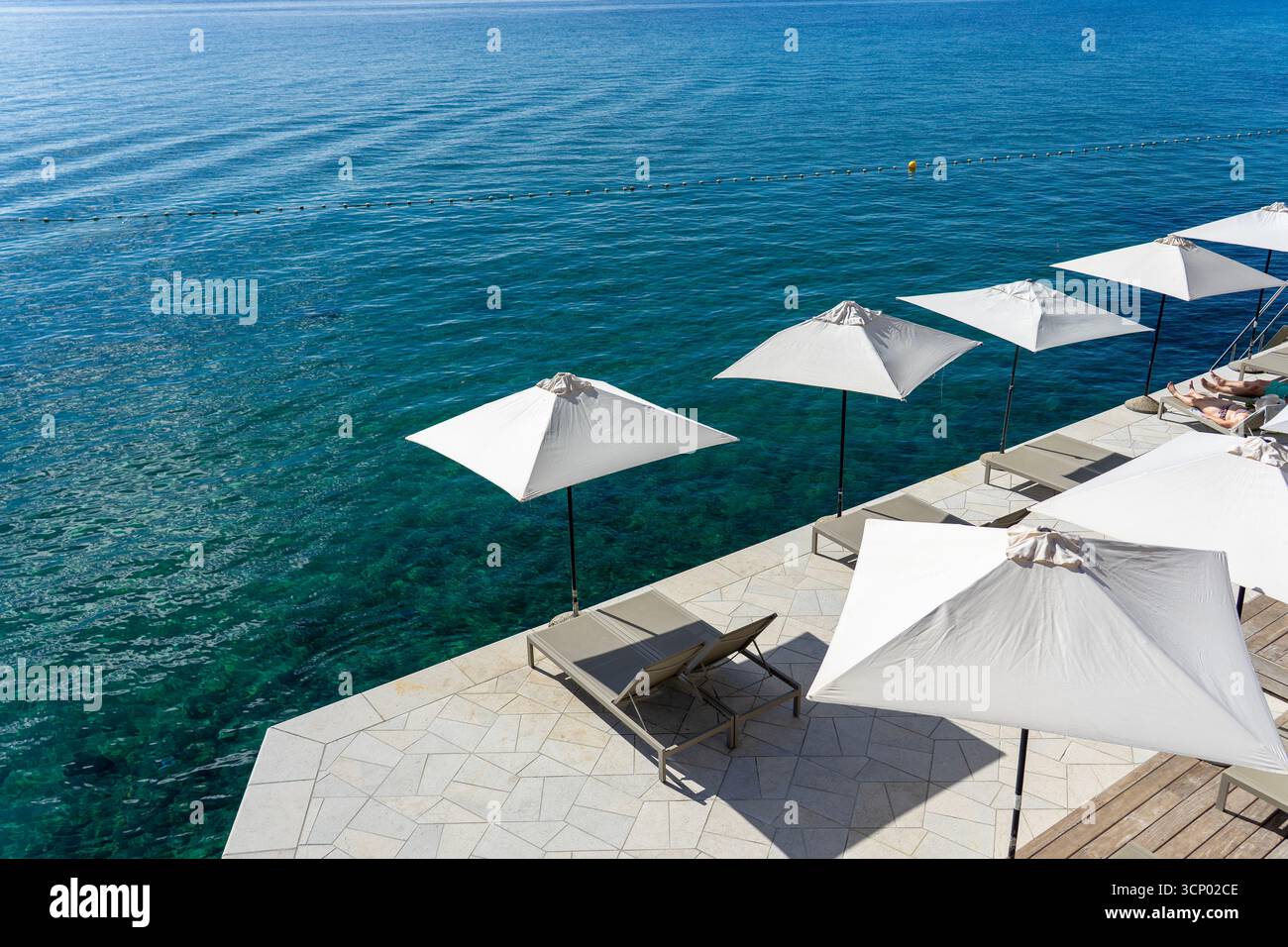 Terrasse am Meer mit Sonnenschirmen und Liegestühlen mit Blick auf das ruhige blaue Meer Opatija Kroatien Stockfoto