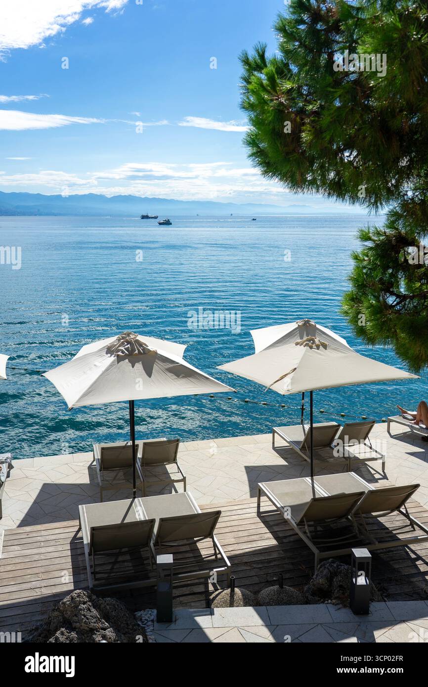 Terrasse am Meer mit Sonnenschirmen und Liegestühlen mit Blick auf das ruhige blaue Meer Opatija Kroatien Stockfoto