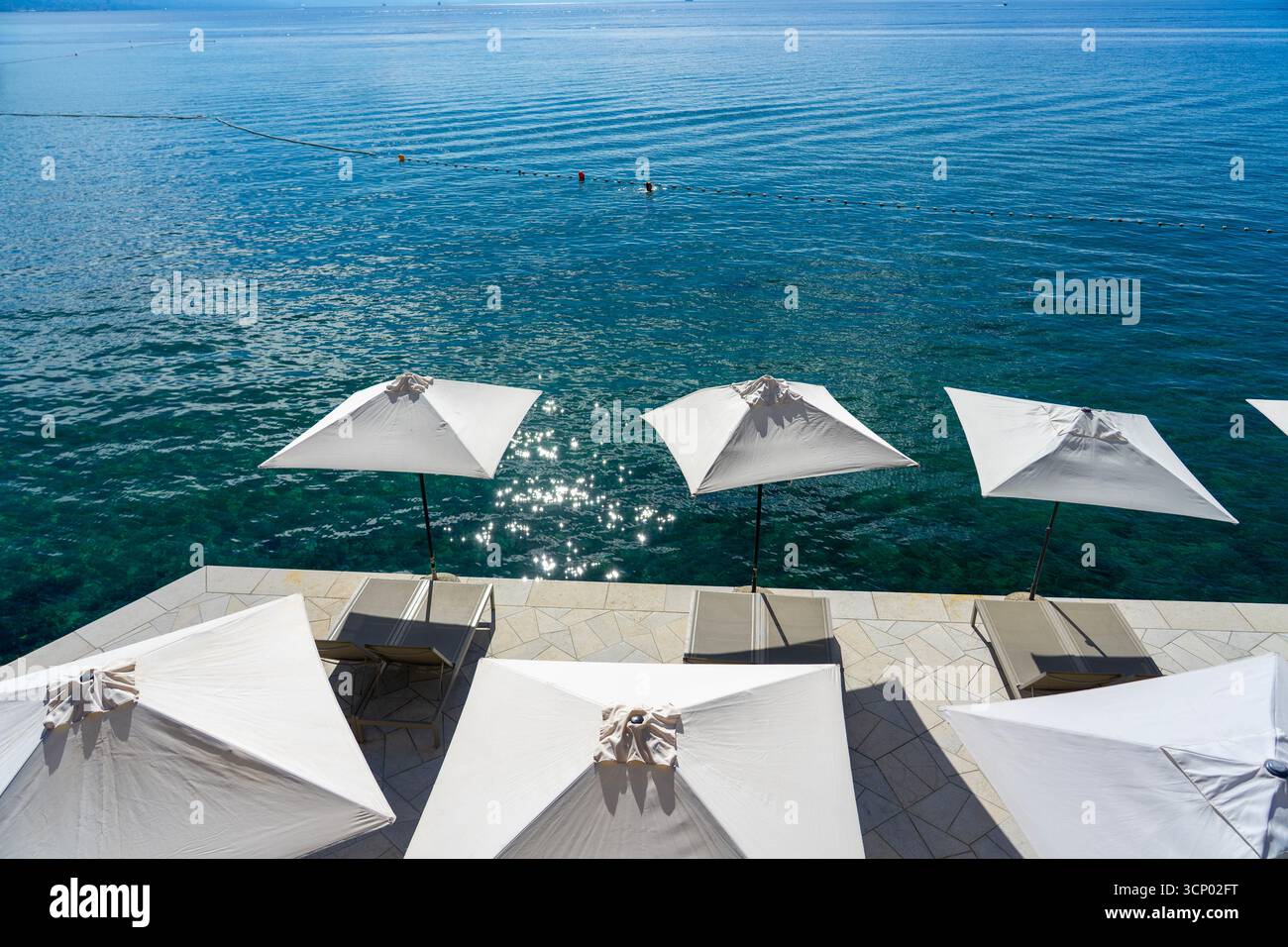 Terrasse am Meer mit Sonnenschirmen und Liegestühlen mit Blick auf das ruhige blaue Meer Opatija Kroatien Stockfoto