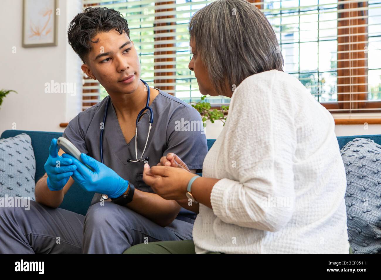 Asiatische Arzthelferin mit Stethoskop und Handschuhen mit Glucometer-kontrollierendem Seniorpatienten Stockfoto