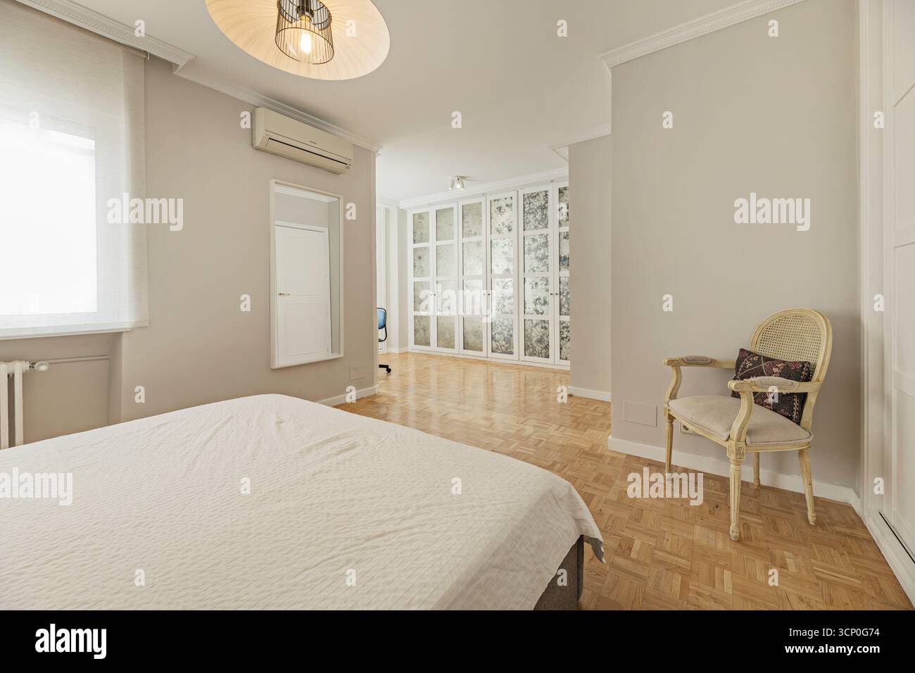 Hauptschlafzimmer mit minimalistischem Kingsize-Bett, indirekter Beleuchtung im Kopfteil und raumhohen Einbauschränken Stockfoto