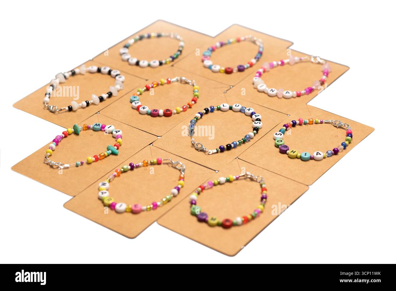Farbenfrohe handgefertigte Kinderarmbänder mit Buchstabenperlen, in denen Namen wie Hanna, Lukas, Sophia, Mia geschrieben werden. Auf Pappkarten ausgestellt, bereit für Geschenkpackung Stockfoto
