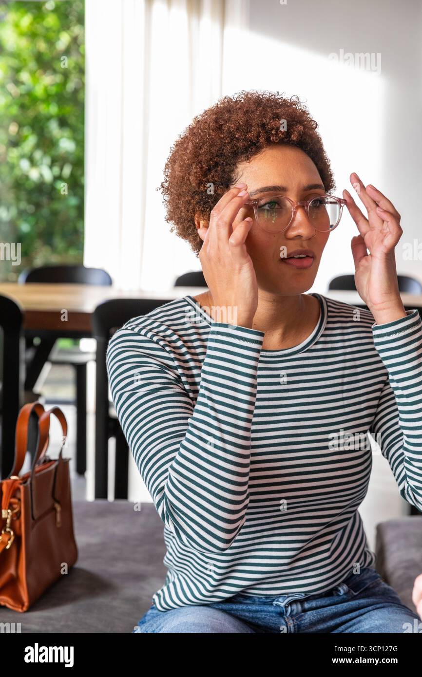 afroamerikanerin passt Brillen an, während sie im Essbereich auf der Bank sitzt Stockfoto