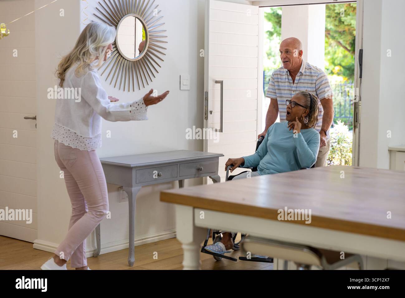 Verschiedene Seniorinnen und Gastfreundinnen begrüßen den Eingang zu Hause mit Rollstuhl und Spiegel Stockfoto