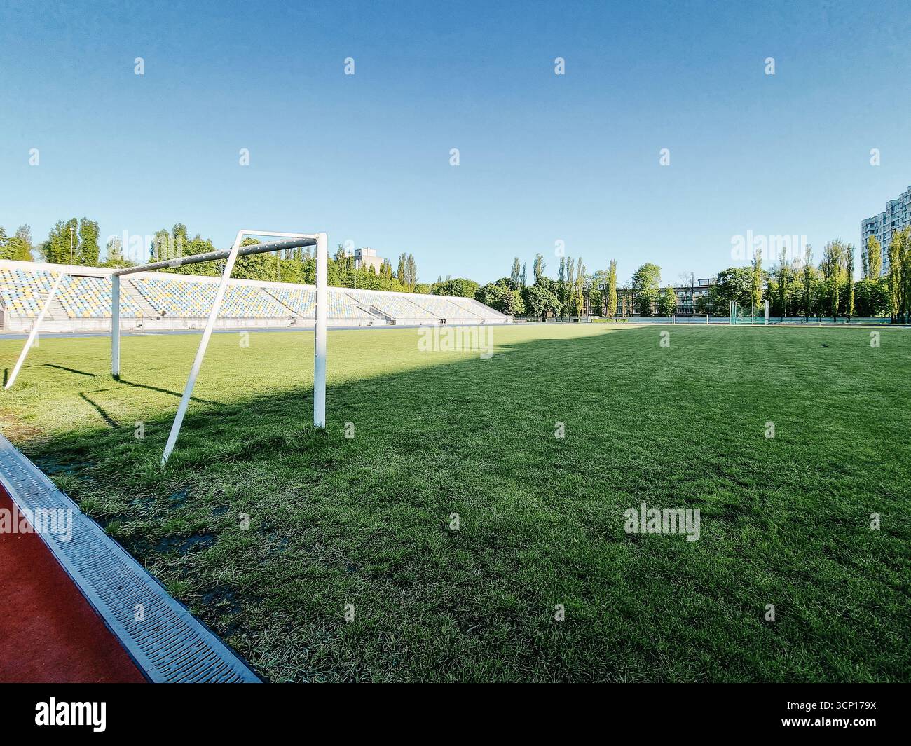 Leeres Fußballfeld am Morgen. Schatten bedeckt die Hälfte des Feldes, großes Tor in der Nähe der Kamera. Stockfoto