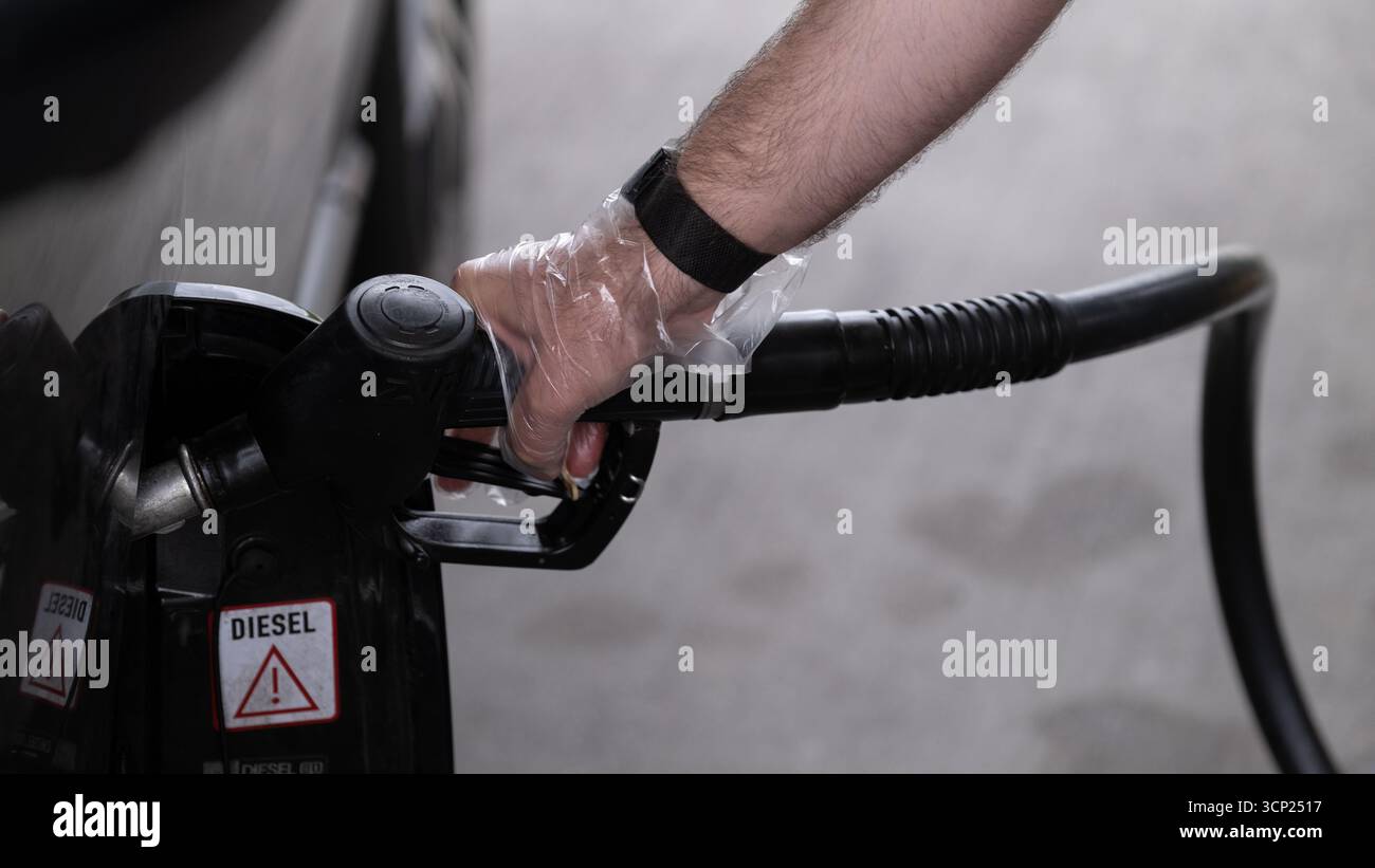 Editorial-Bild eines Mannes, der an einer Tankstelle in Polen ein Fahrzeug mit Diesel betankt, September 2025. Die Hand trägt einen Einweghandschuh zur Hygiene Stockfoto