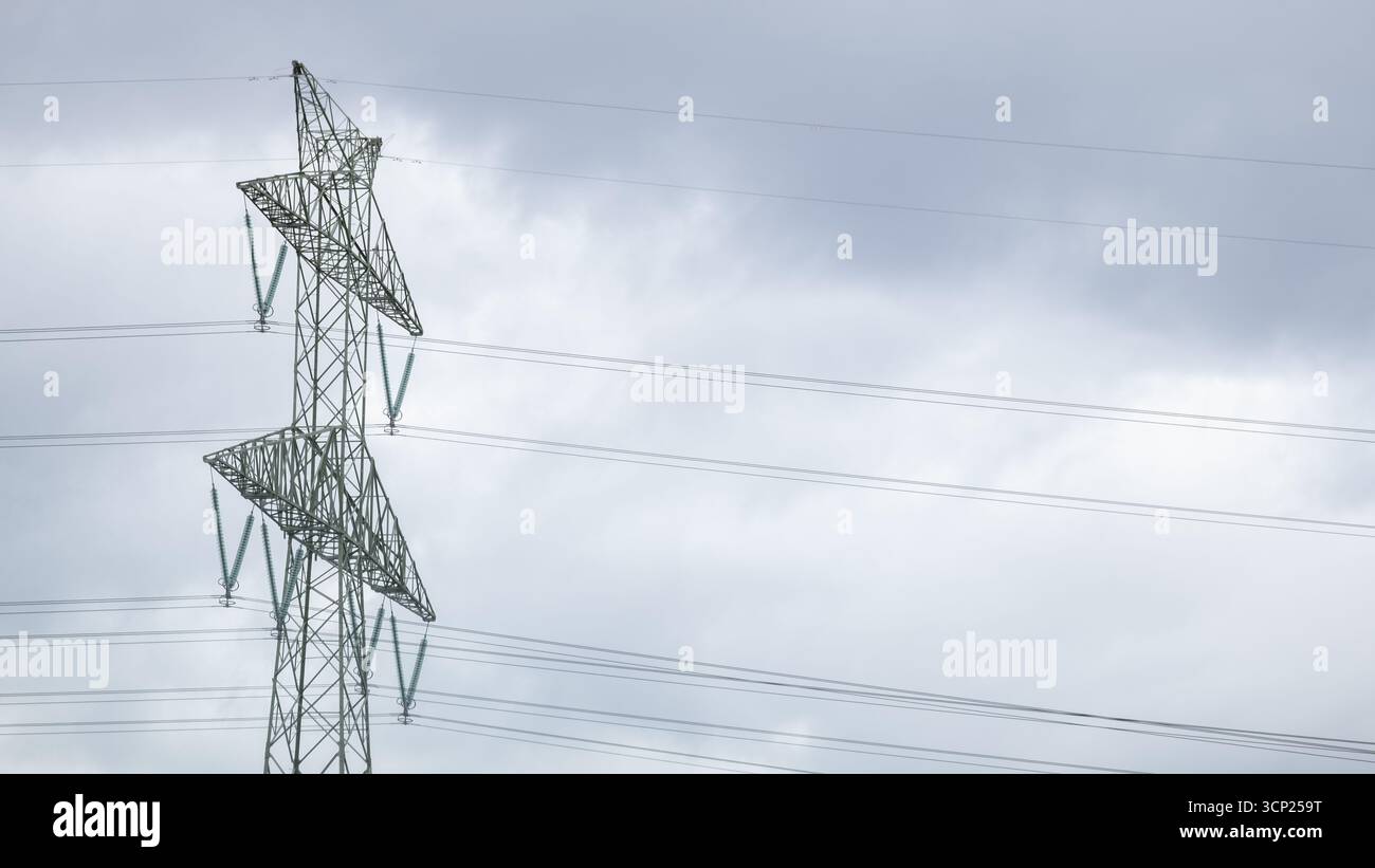 Nahaufnahme eines Hochspannungsnetzturms mit mehreren Kabeln auf bewölktem Himmel. Das Bild zeigt die Energieinfrastruktur, die Elektrizität Stockfoto