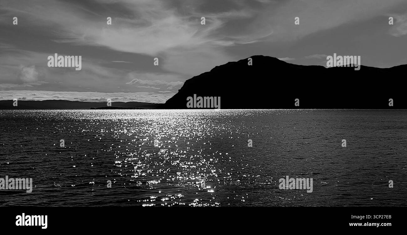 Das klare blaue Wasser in Neufundlands Bay of Islands glitzert im Sonnenlicht mit einer markanten Bergsilhouette in der Ferne. In Schwarzweiß Stockfoto