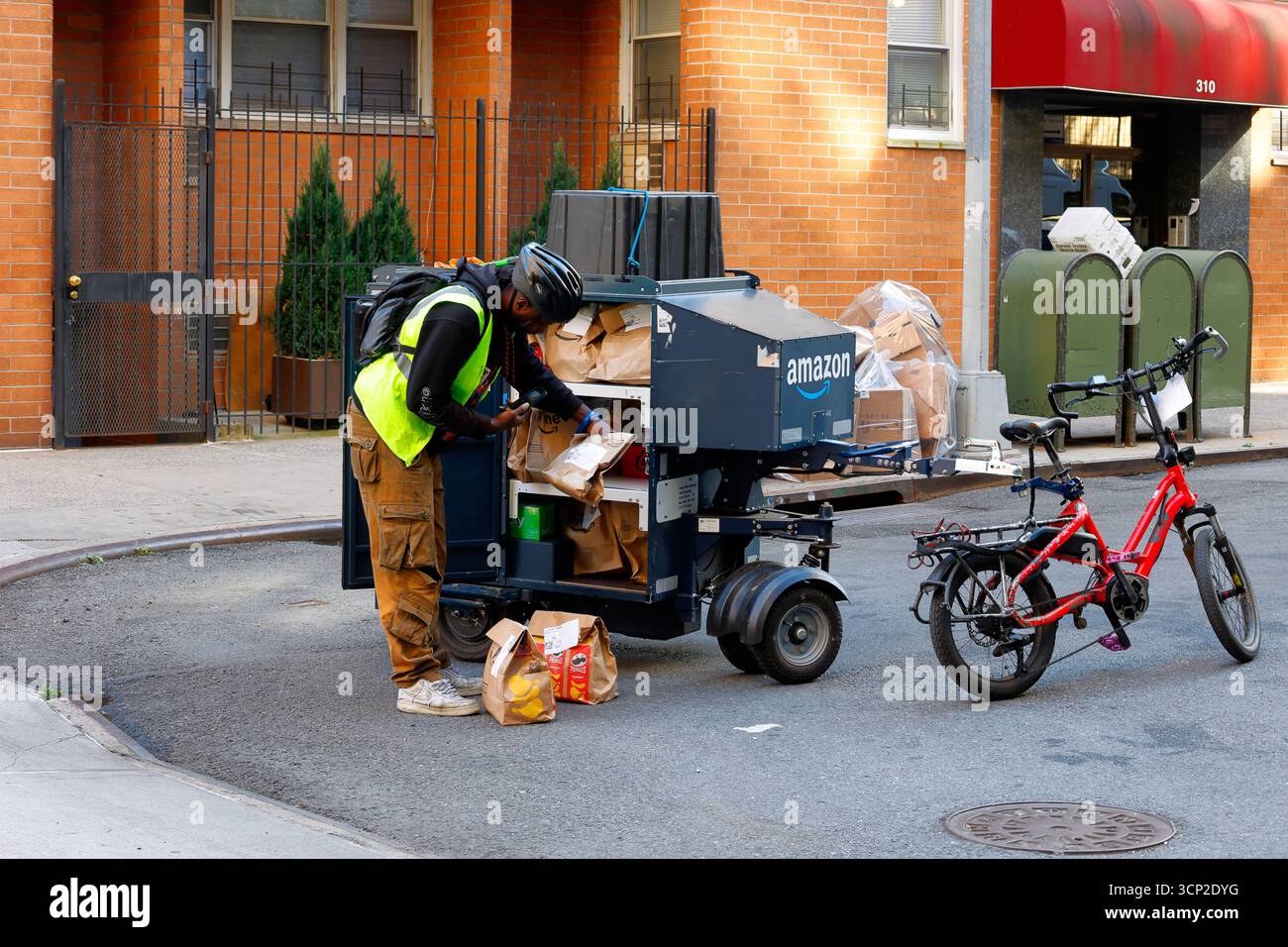 Ein Mitarbeiter scannt ein Lieferpaket am selben Tag, das in einem an einem E-Mail-Gerät angebrachten K Royle Utility Electric Anhänger mit der Marke Amazon transportiert wird. Stockfoto