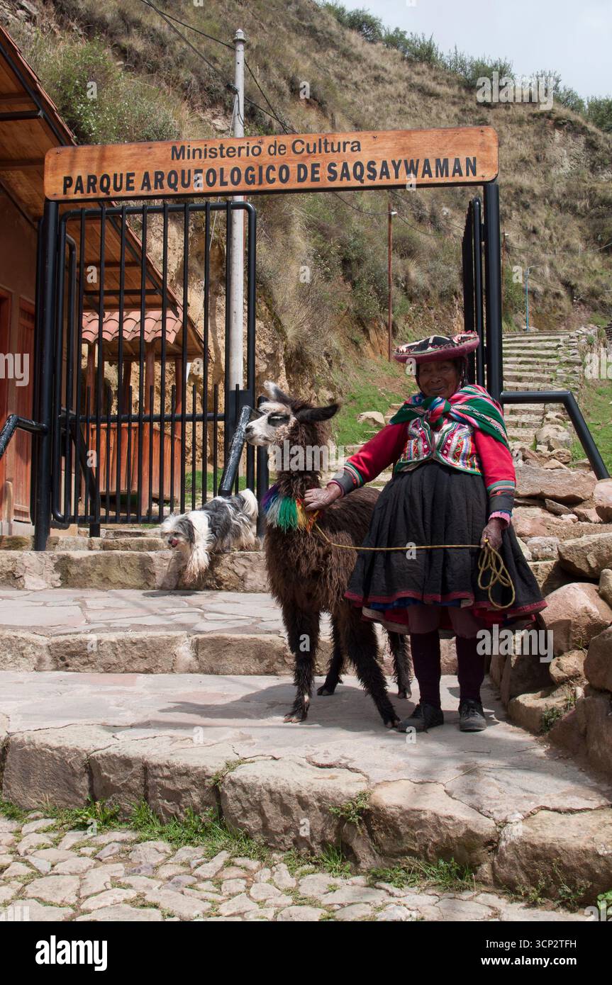 Ruinas en Sacsayhuamán, fortaleza inca en Cusco. Mujer con ropas tradicionales y una alpaca a las puertas del parque para tomar foto con ella. Stockfoto