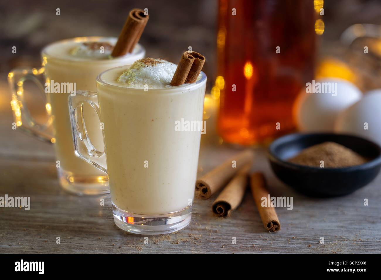 Zwei Gläser Egg Nog mit Rum, Muskatnuss, Zimtstangen und Eiern im Hintergrund Stockfoto